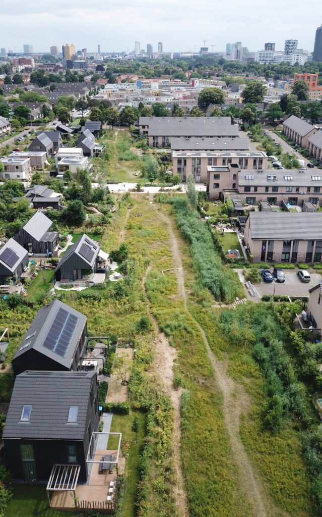 luchtfoto zelfbouw woningen in houtbouw aan wadi in groene woonwijk met panorama van stad Eindhoven aan horizon